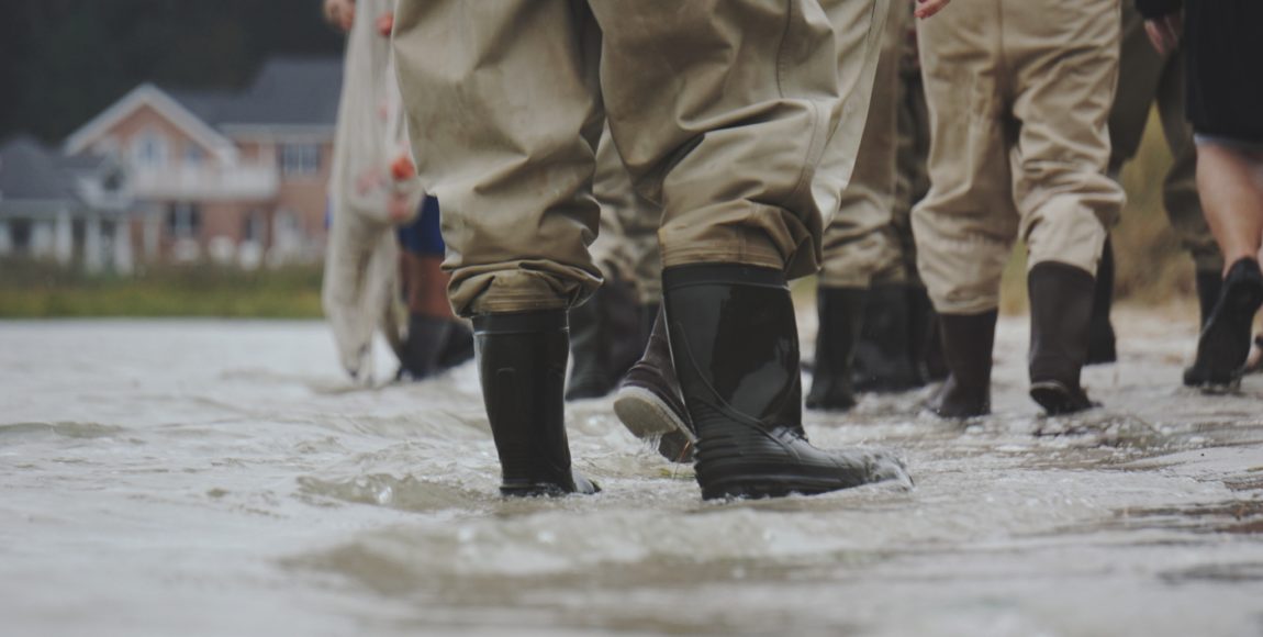 Individuals with rain boots walking down a flooded street.
